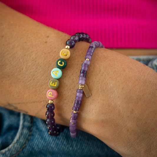 A person is wearing two bracelets on their wrist, one with colorful beads and the other with purple beads.